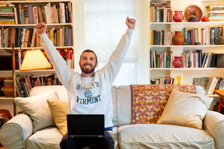 male student arms raised in excitement sitting on couch