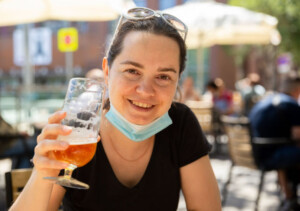 Woman in protective medical mask with glass of beer at a street bar