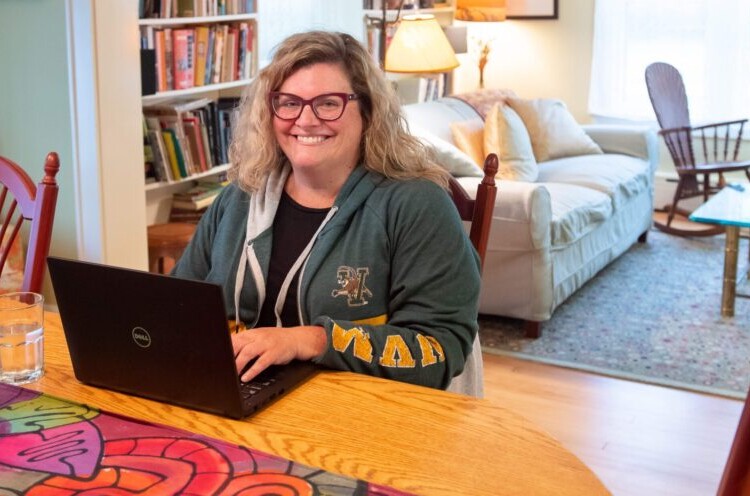 adult woman working at a desk at home wearing UVM sweatshirt