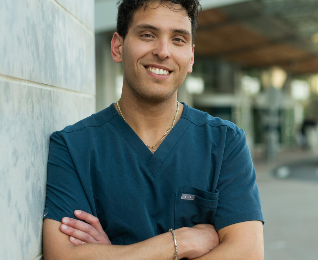 A smiling Post-Baccalaureate Pre-Medical student outside of a hospital