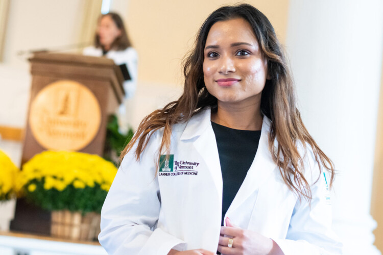 Woman wearing a white coat with a woman at a podium in the background