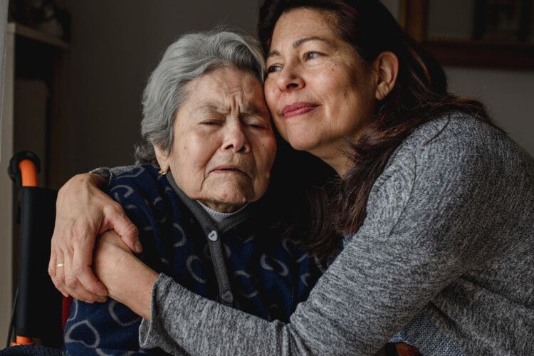 Person holding a seated elderly person in a compassionate way