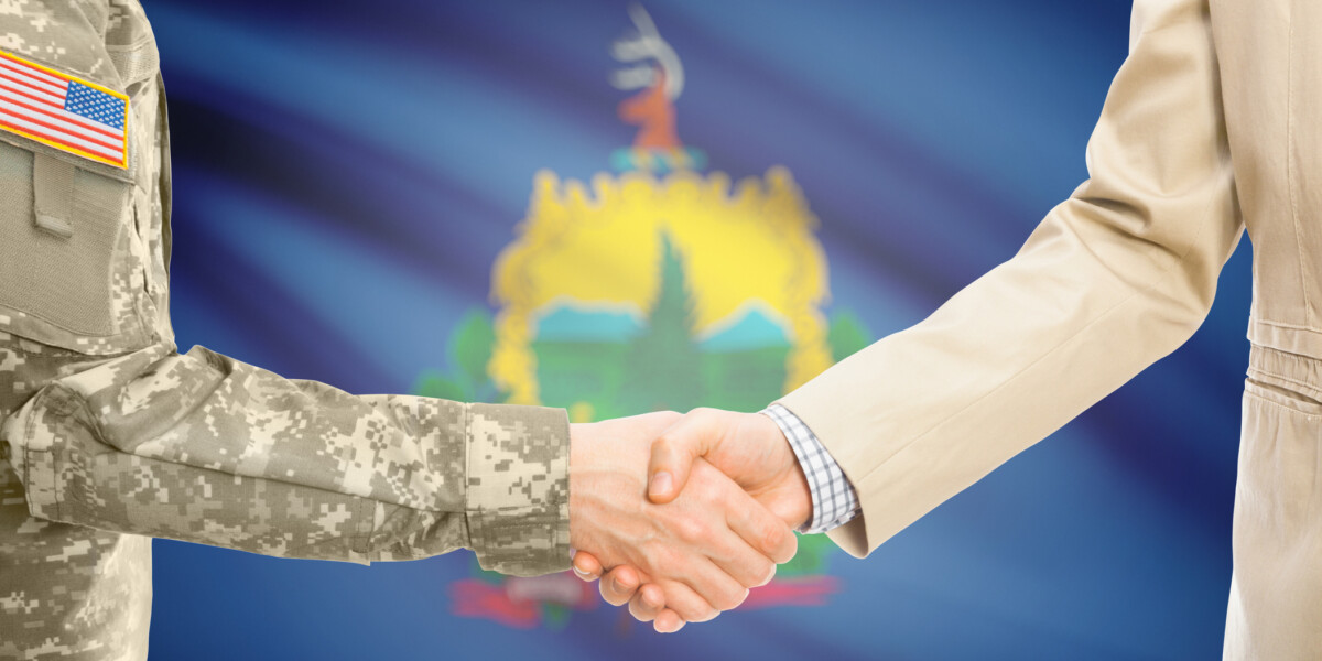 Handshake between military person and civilian in front of Vermont state flag.