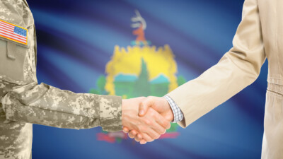 Handshake between military person and civilian in front of Vermont state flag.