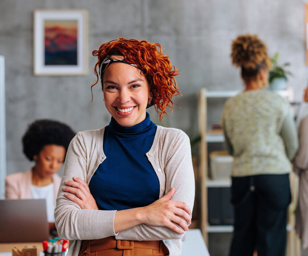 Business woman smiling and standing in an office setting with arms crossed