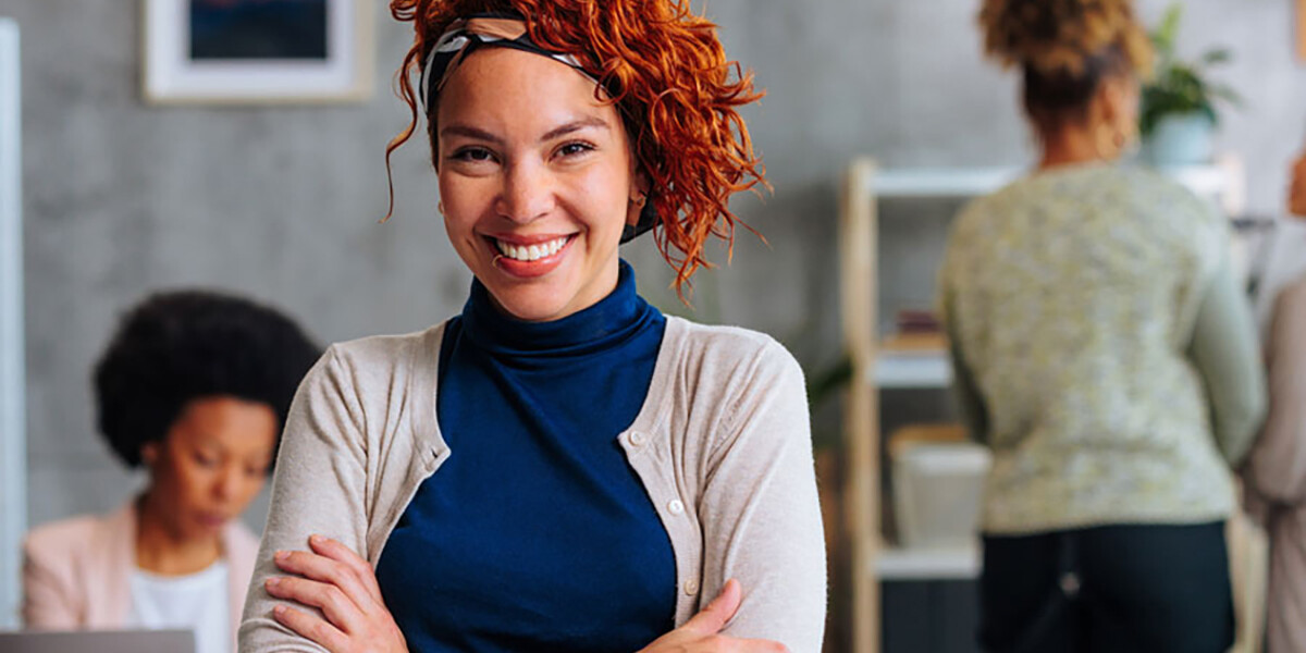 Business woman smiling and standing in an office setting with arms crossed