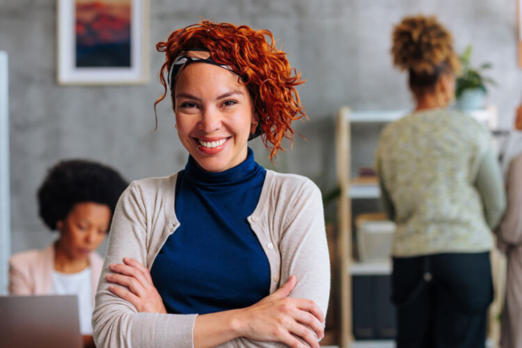 Business woman smiling and standing in an office setting with arms crossed