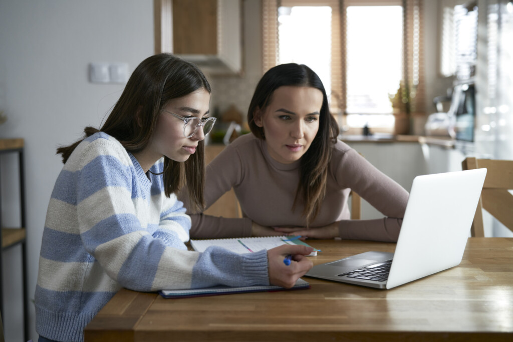 Mother with teenager daughter looking at a laptop at the kitchen table. 