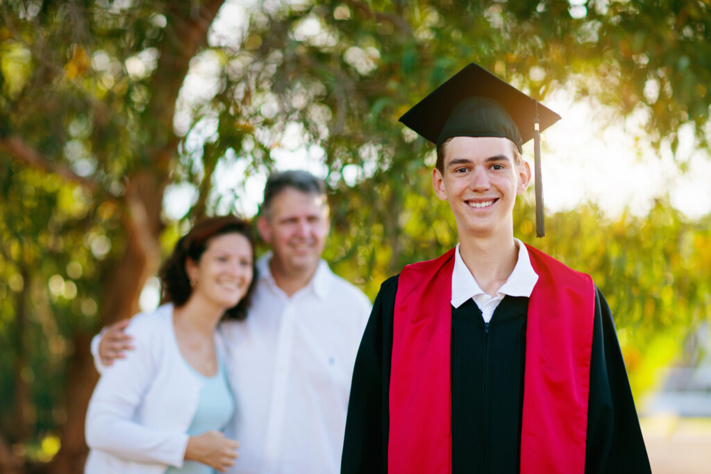 School or college graduation ceremony. Young man in gown and cap, with his family in the background.