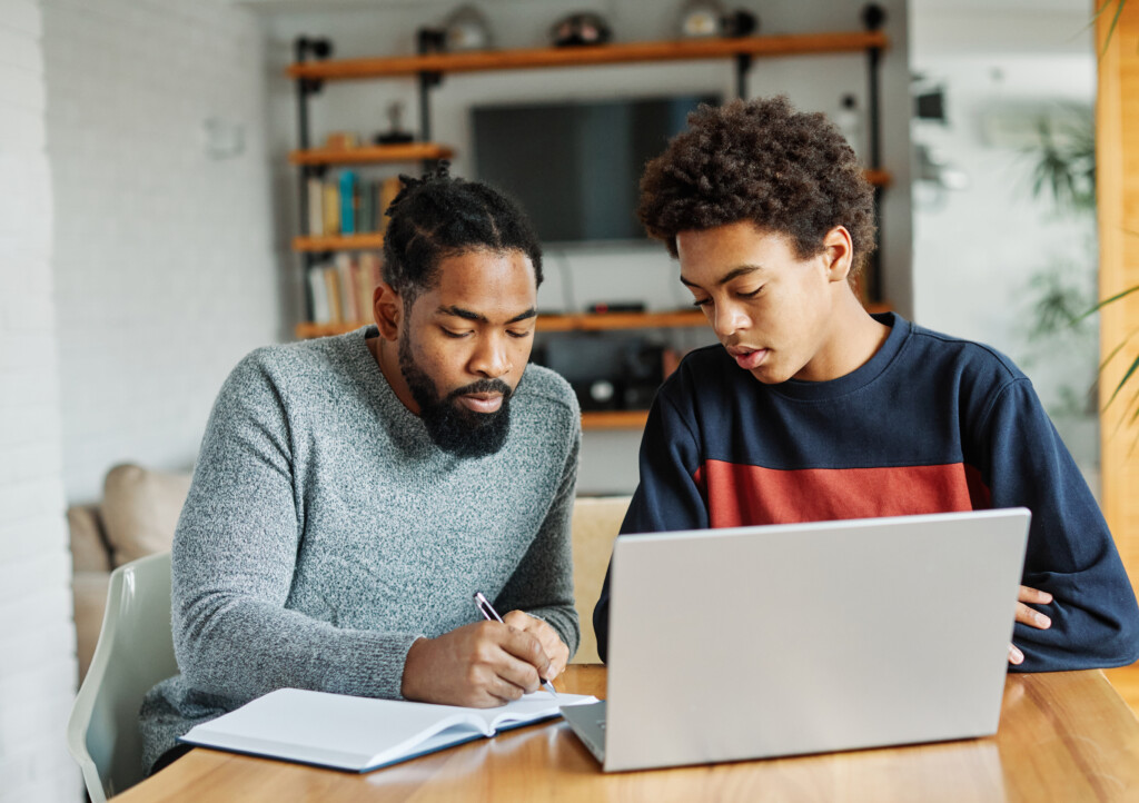 Dad and son looking at papers on desk with a laptop in front of them on the desk.
