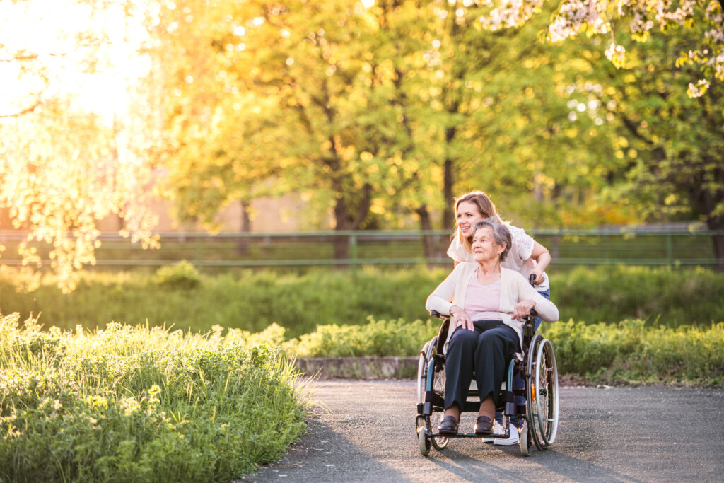End-of-Life Doula Certificate portfolio at University of Vermont. Elderly woman in wheelchair with an end-of-life doula, outside walking along a pathway in a park.