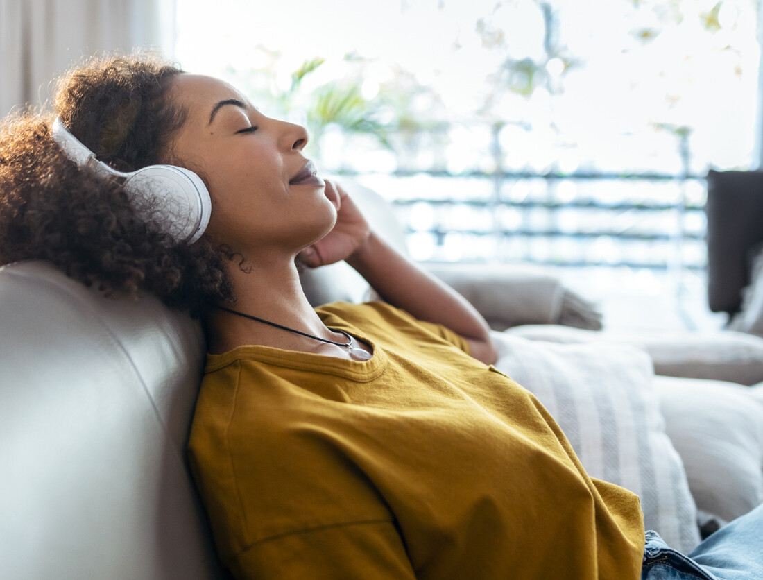 Human sitting back on a couch wearing headphones in a mustard-colored shirt.