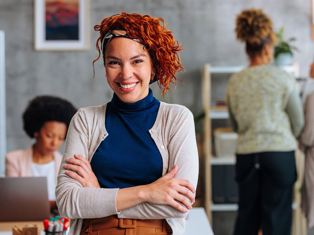 Business woman smiling and standing in an office setting with arms crossed
