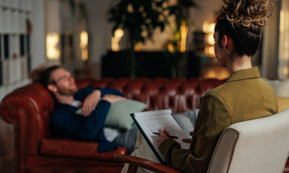 A young adult female therapist uses her notebook to take notes as she listens to her male client.