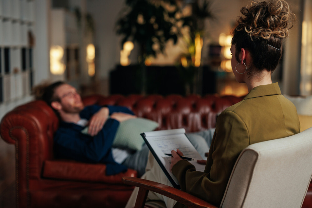 A young adult female therapist uses her notebook to take notes as she listens to her male client.