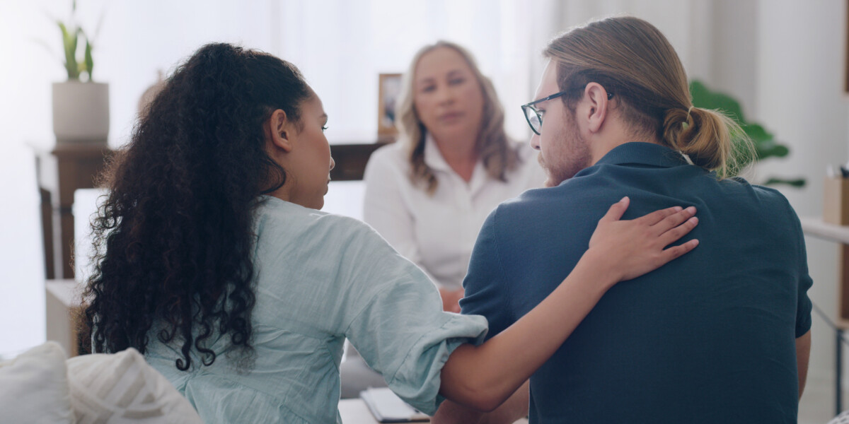 A woman and a man in a therapist's office receiving support and guidance from a psychologist or social worker during a counseling session.