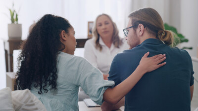 A woman and a man in a therapist's office receiving support and guidance from a psychologist or social worker during a counseling session.