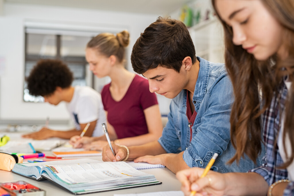 Group of four high school students writing on notebooks on a table i a classroom.
