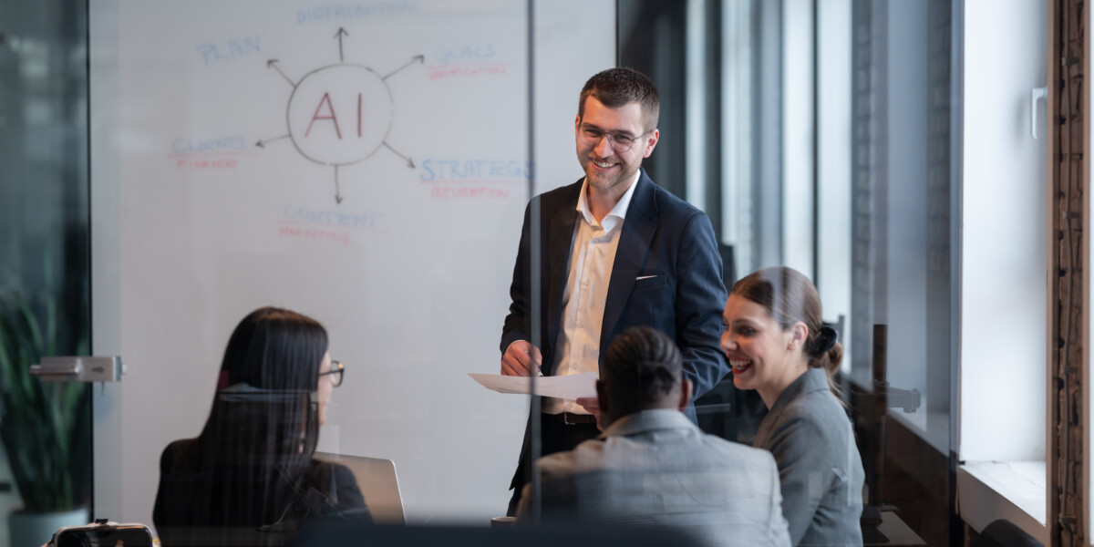 Businessman in a dark suit presenting to colleagues in a glass-walled meeting room, with an AI diagram on the whiteboard.